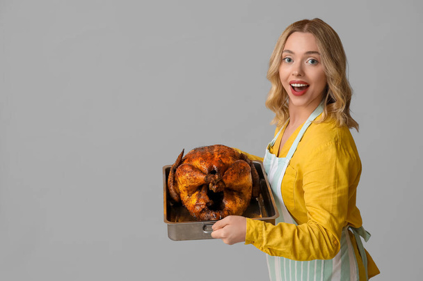 Mujer joven emocionada con sabroso pavo al horno sobre fondo gris. Celebración del Día de Acción de Gracias - Foto, imagen