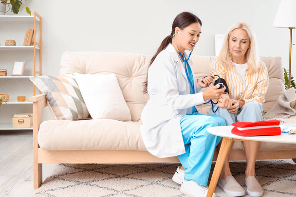 Médico femenino midiendo la presión arterial del paciente en casa - Foto, imagen