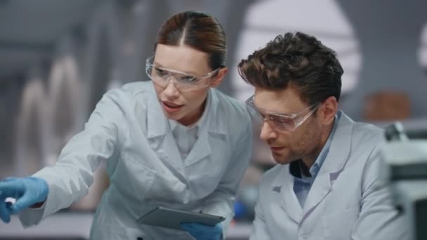 Biotechnology specialists researching medicines in innovation lab close up. Skilled woman scientist teaching man intern showing drugs sample. Two professional researcher discussing science experiment. - Footage, Video