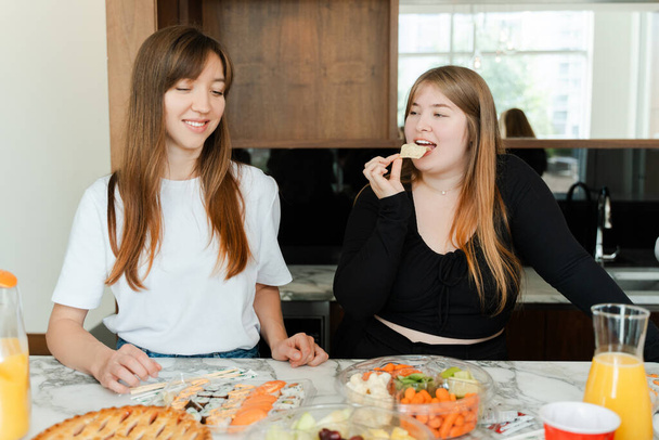 Two girls sitting at the table at birthday party celebration. Woman tasting snacks, enjoying time with friends. People lifestyle concept - Photo, Image