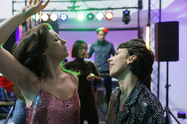Беззаботные девушки танцуют и празднуют вместе на вечеринке в ночном клубе. Молодые женщины делают энергичные движения на танцполе во время отдыха на общественном собрании в клубе - Фото, изображение