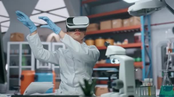 VR gözlüklü doktor artırılmış gerçeklik simülasyonunu kontrol ediyor modern laboratuvarda araştırma yapıyor. Kadın bilim adamı ellerle görünmez arayüzü hareket ettiriyor. Gözlüklü bir araştırmacı siber uzayda çalışıyor - Video, Çekim