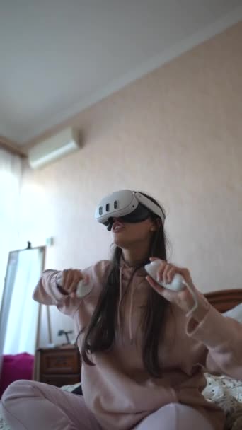 Rózsaszín pizsamában egy gyönyörű fiatal hölgy fedezi fel a virtuális valóság játékát. Kiváló minőségű 4k felvételek - Felvétel, videó