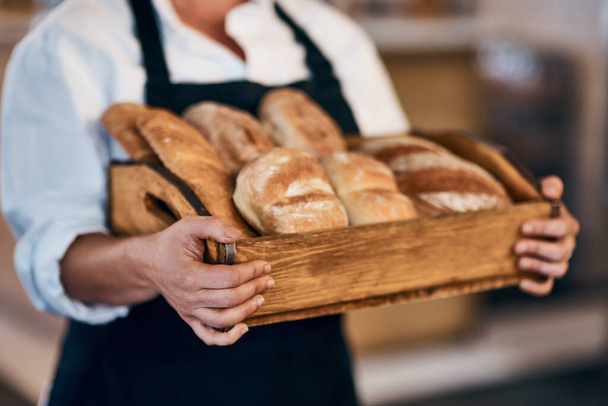 Horneado por la misma panadera. una mujer sosteniendo una selección de panes recién horneados en su panadería - Foto, imagen