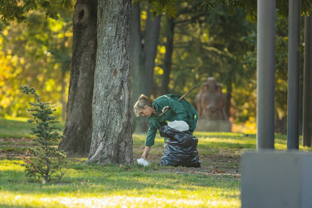 29 september 2023, Belgrade, Serbia - woman cleaner in the autumn city park undertake of plastic garbage, telephoto shot - Фото, изображение