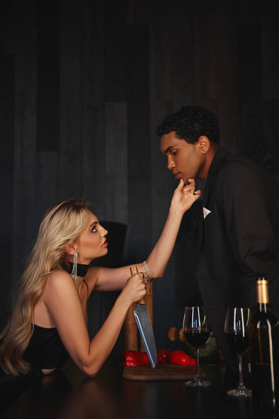 hombre afroamericano guapo en traje elegante mirando a su hermosa novia sosteniendo cuchillo - Foto, Imagen