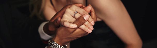 обрізаний вид рук молодої багаторасової пари з заручинним алмазним кільцем на пальці, банер - Фото, зображення