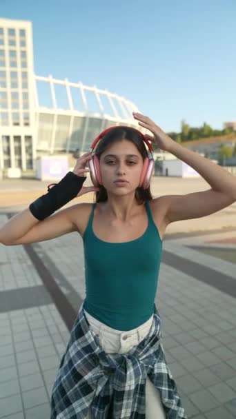 Avec des écouteurs dans les oreilles, une charmante jeune femme danse dans la rue par une journée ensoleillée. Images 4k de haute qualité - Séquence, vidéo