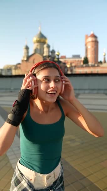 Sur la place de la ville, une jeune femme dynamique danse avec un casque. Images 4k de haute qualité - Séquence, vidéo