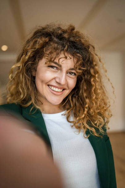 Una mujer caucásica mujer feliz seguro de pie interior en la cafetería con el pelo rizado sonrisa persona real copia espacio autorretrato selfie UGC usuario contenido generado - Foto, imagen