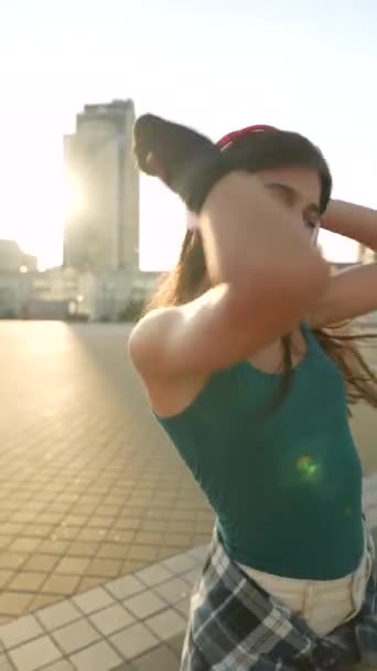 Op een zonnige dag danst een mooie jongedame terwijl ze buiten een koptelefoon draagt. Hoge kwaliteit 4k beeldmateriaal - Video
