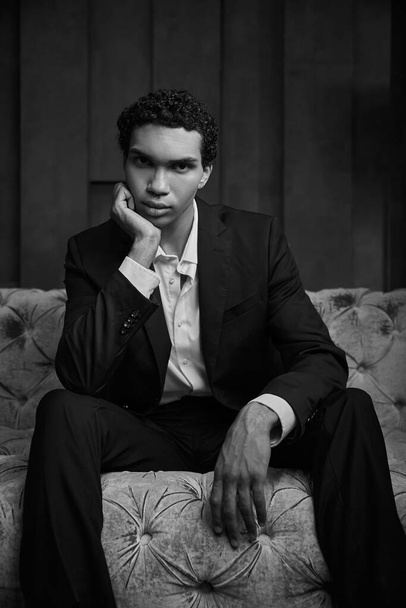 foto preto e branco de homem americano africano elegante sentado no sofá e olhando para a câmera - Foto, Imagem