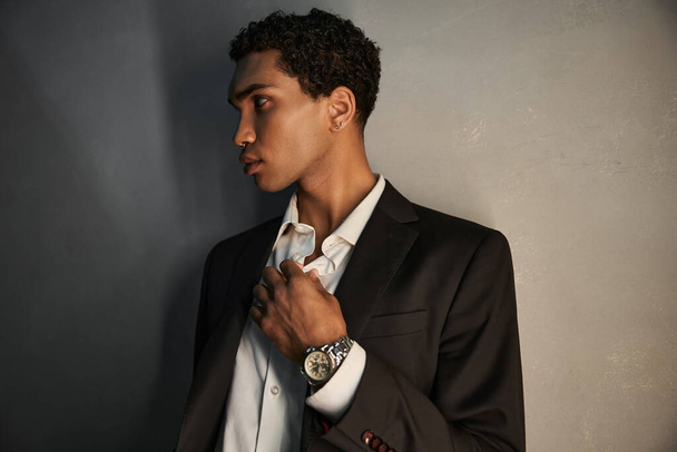 good looking young african american man with accessories in black suit posing and looking away - Fotó, kép