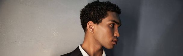 atractivo joven afroamericano hombre con accesorios en traje negro posando y mirando hacia otro lado, pancarta - Foto, Imagen