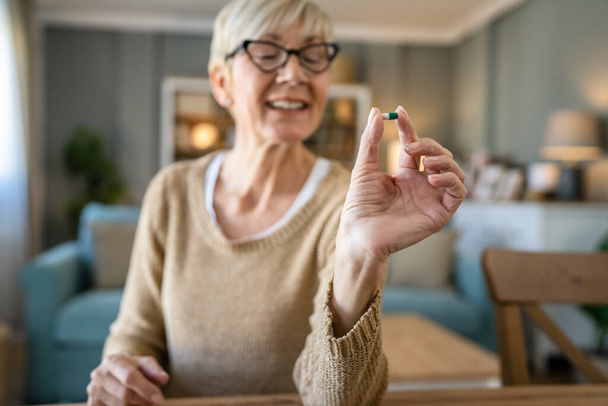 Een oudere blanke vrouw oude vrouw neemt medicijnen of aan te vullen vitamine thuis echte mensen gezondheidszorg concept - Foto, afbeelding