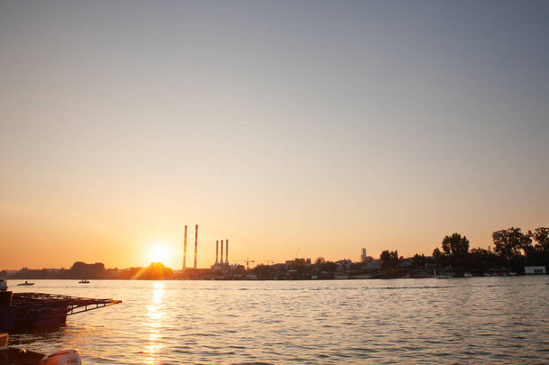 Panorama del río reka Sava en Belgrado, en Serbia, con un paisaje industrial de Europa del Este con fábricas rojas y blancas y chimeneas contaminando, al atardecer, durante una tarde soleada. - Foto, Imagen