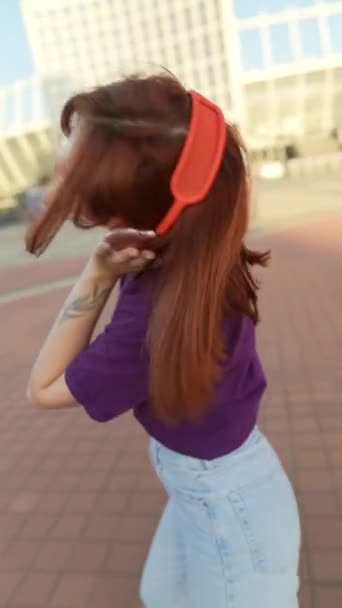 La impresionante mujer pelirroja, con auriculares puestos, está bailando en la plaza del centro de la ciudad. Imágenes de alta calidad 4k - Metraje, vídeo