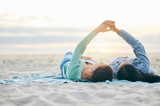 Love, beach and lesbian couple on blanket together, holding hands on sand and sunset holiday adventure. Lgbt women, bonding and relax on ocean vacation with romance, pride and happy lying in nature - Photo, Image