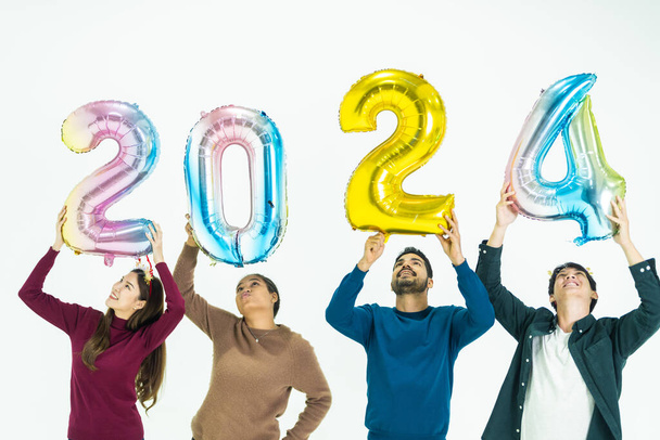 grupo de personas que sostienen globos de colores de fantasía burbuja del número 2024 para el nuevo año. hombres y mujeres de pie sobre un fondo blanco. celebración de la fiesta feliz año nuevo - Foto, imagen