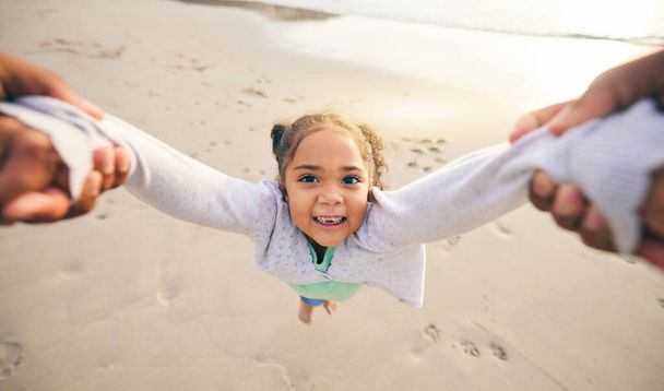 Happy, swinging and portrait of child at the beach for travel, support and fun. Spinning, smile and summer with girl and holding hands with family together for vacation, trust and seaside holiday. - Photo, Image