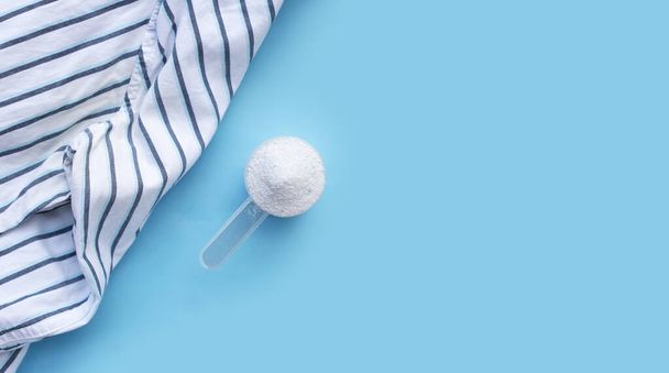 Detergent powder in measuring spoon with cloth before washing. Laundry concept. - Foto, afbeelding