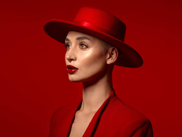 Vision, fashion and a model woman on a red studio background for elegant or trendy style. Aesthetic, art and hat with a young female person looking edgy or classy in a suit or unique clothes. - Foto, imagen