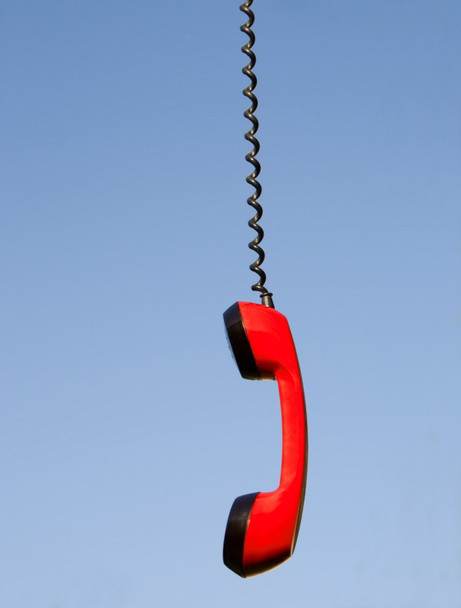 Red phone handset hanging against blue sky - Фото, изображение