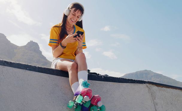 Smile, phone and music with woman and roller skates for skating, streaming and social media app. Technology, headphones and sports with girl in skate park for internet, mobile radio and fitness. - Photo, Image