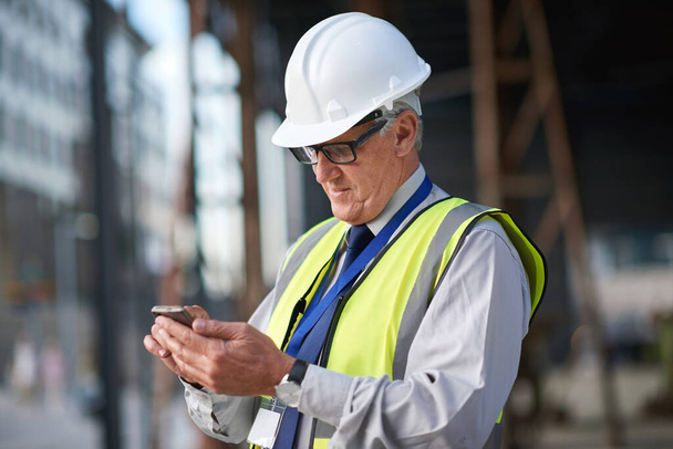 Építőipar, mérnök és ember telefonnal kommunikálni az épület projektmenedzsment. Vezető vállalkozó személy gépelés okostelefonon építőmérnöki kapcsolat, biztonság vagy fejlesztés a helyszínen. - Fotó, kép