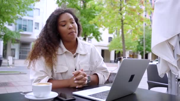 Νεαρή μαύρη γυναίκα έχει τηλεδιάσκεψη στη βεράντα ενός μπαρ. Αφροαμερικανός που μιλάει σε εξωτερικούς χώρους με λάπτοπ - Πλάνα, βίντεο