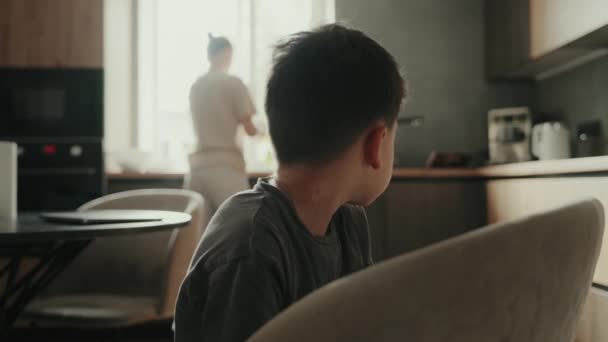Маленький хлопчик розмовляє зі своєю матір'ю про те, як він був у школі, поки вона готує на кухні. - Кадри, відео