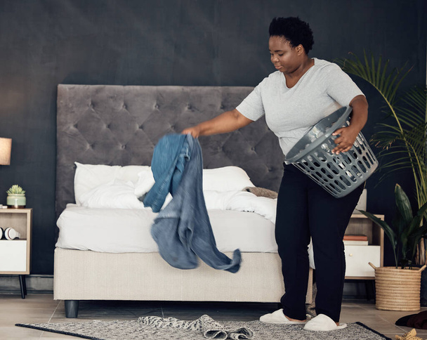 Musta nainen, vaatteita kori ja puhdistus makuuhuone, järjestää sotku hygieniaa ja vieraanvaraisuutta. Naispuolinen henkilö, siivooja ja siivooja, kiireinen pyykin kanssa ja ylläpito aamurutiinilla. - Valokuva, kuva