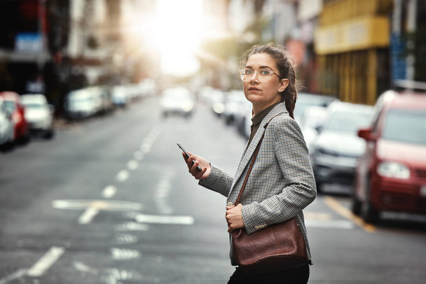 Phone, portrait of woman and cross street for journey, sunset commute and social media on internet. Mobile, consultant and person walk in city on smartphone for business, cbd travel and lens flare. - Photo, Image