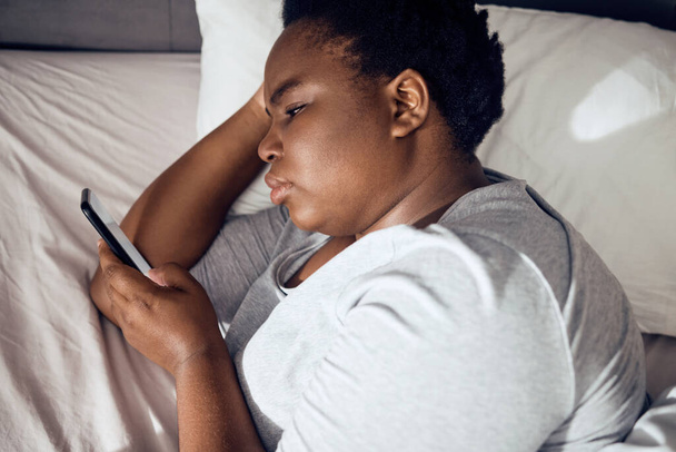 Schlaflosigkeit, morgendliche oder schwarze Frau im Bett mit Handy für soziale Medien, die im Raum für Sucht zu Hause liegt. Stress, einsame oder traurige Person, die online liest, um auf mobiler App im Schlafzimmer mit Depressionen zu scrollen. - Foto, Bild