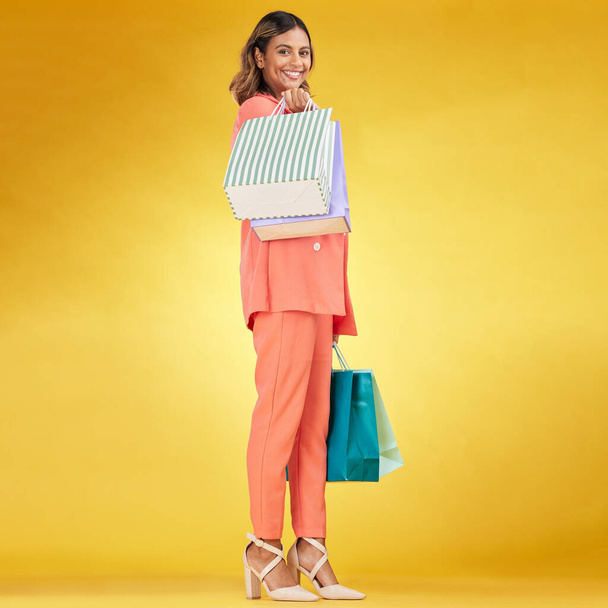 Portrait, happy woman and shopping bag in studio for clothes, retail deal and financial freedom on yellow background. Indian customer, gift bags and discount from fashion store, sales and promotion. - Zdjęcie, obraz