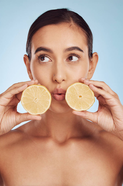 Woman, hands and lemon for skincare detox, diet or collagen against a blue studio background. Female person or model holding organic citrus fruit for natural nutrition, anti aging or facial treatment. - Photo, Image