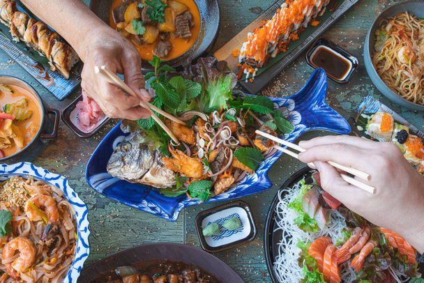 ręce z pałeczkami jedzącymi tajskie jedzenie z bliska, sałatki i wok, azjatyckie jedzenie, widok z góry. Kuchnia japońska i tajska. - Zdjęcie, obraz