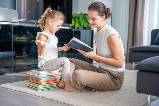 Young mother is reading a book to her smiling daughter. High quality photo - Photo, Image