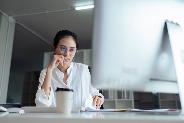 młody Azji bizneswoman księgowy w biuro biurko patrzeć na komputer ekran myśleć o problem rozwiązanie. - Zdjęcie, obraz