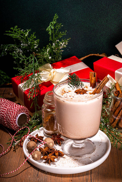 Yeni yıl Noel kremalı baharatlı kokteyl eggnog. Sütlü, yumurtalı, romlu, tarçınlı ve hindistan cevizli sıcak kış içeceği ahşap arka planda Noel süsüyle - Fotoğraf, Görsel