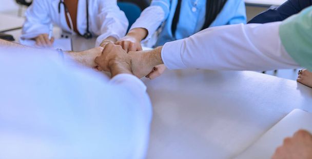 Eine Gruppe von Ärzten und eine Krankenschwester legen ihre Hände an einen Tisch und zeigen damit die unerschütterliche Teamarbeit und Solidarität, die ihre gemeinsamen Bemühungen im Gesundheitsbereich antreiben..  - Foto, Bild