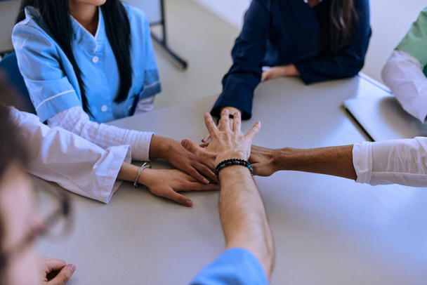 Egy csapat orvos és egy egészségügyi nővér összefogja a kezüket az asztalon, bemutatva a megingathatatlan csapatmunkát és szolidaritást, amely az egészségügy területén közös erőfeszítéseik mozgatórugója..  - Fotó, kép