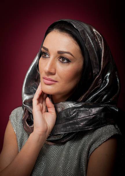Attractive brunette woman in gray blouse and headscarf posing dramatic on purple background. Female art portrait, studio shot. Genuine natural girl with sad smile. Woman in Virgin Mary pose - Photo, Image
