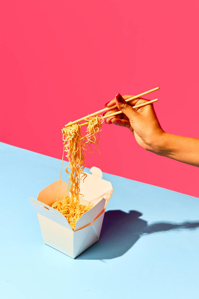 Lähikuva kuva tunnistamaton tyttö syö paperilaatikosta nuudelit, pikaruokaa vastaan vihreä-vaaleanpunainen tausta. Käsite ruoka, katu ruoka, toimitus, ravintola menu, catering. Kopioi tilaa. Ilmoitus - Valokuva, kuva