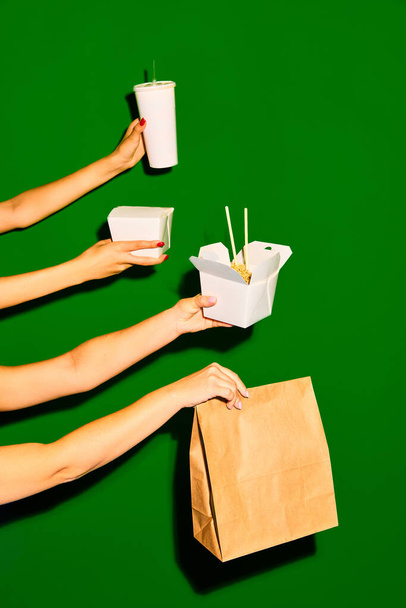 Πάρ 'το από δω. Κοντινό πλάνο εικόνα των γυναικείων χεριών κρατά χάρτινο κουτί και τσάντα και ένα ανοιγμένο κουτί με noodles σε πράσινο φόντο. Έννοια του fast food, street food, παράδοση, μενού, catering. Αντιγραφή χώρου. - Φωτογραφία, εικόνα