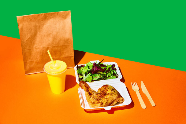 Close-up afbeelding van geopende papieren doos met salade en gebakken kip en sap in papieren beker tegen oranjegroene achtergrond. Concept van fast food, street food, levering, menu, catering. Begrepen, ruimte. Steun - Foto, afbeelding