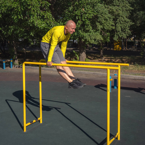 O homem realiza um exercício em bares paralelos em um campo de esportes de rua em um dia ensolarado de verão. Estilo de vida saudável - Foto, Imagem
