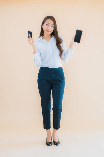 Porträt schöne junge Business-asiatische Frau mit Telefon und Kreditkarte auf farbigem Hintergrund - Foto, Bild