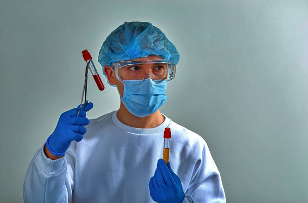 Arzt in Maske führt Bluttest auf Coronavirus COVID19, HIV, Ebola oder jede andere gefährliche Infektion durch. Arztporträt, verschwommener medizinischer Hintergrund, Vorlage, Tapete. Coronavirus-Krankheit  - Foto, Bild