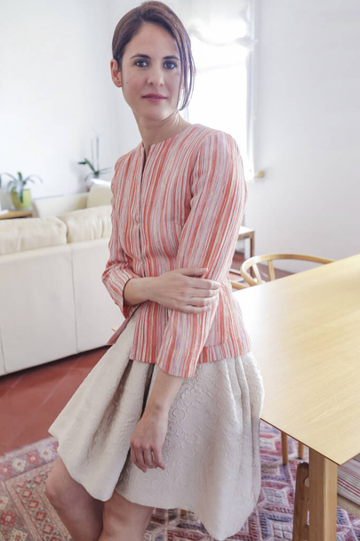 Pretty fashion model wearing pink shirt and beige skirt while standing at home and looking at camera - Photo, Image